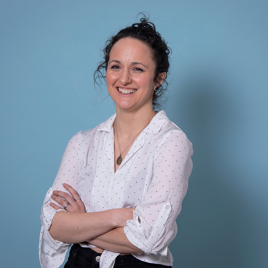 white woman with brown hair in a bun standing with her arms crossed in a white button down blouse.