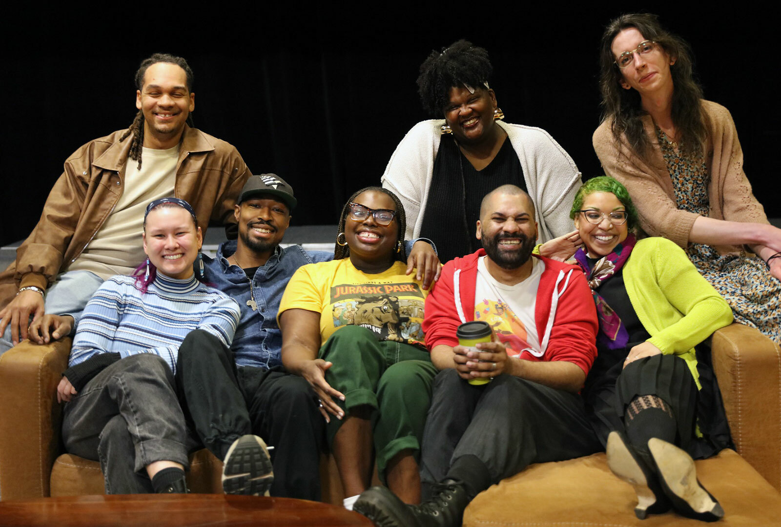 Eight smiling people gathered close together on a sofa.