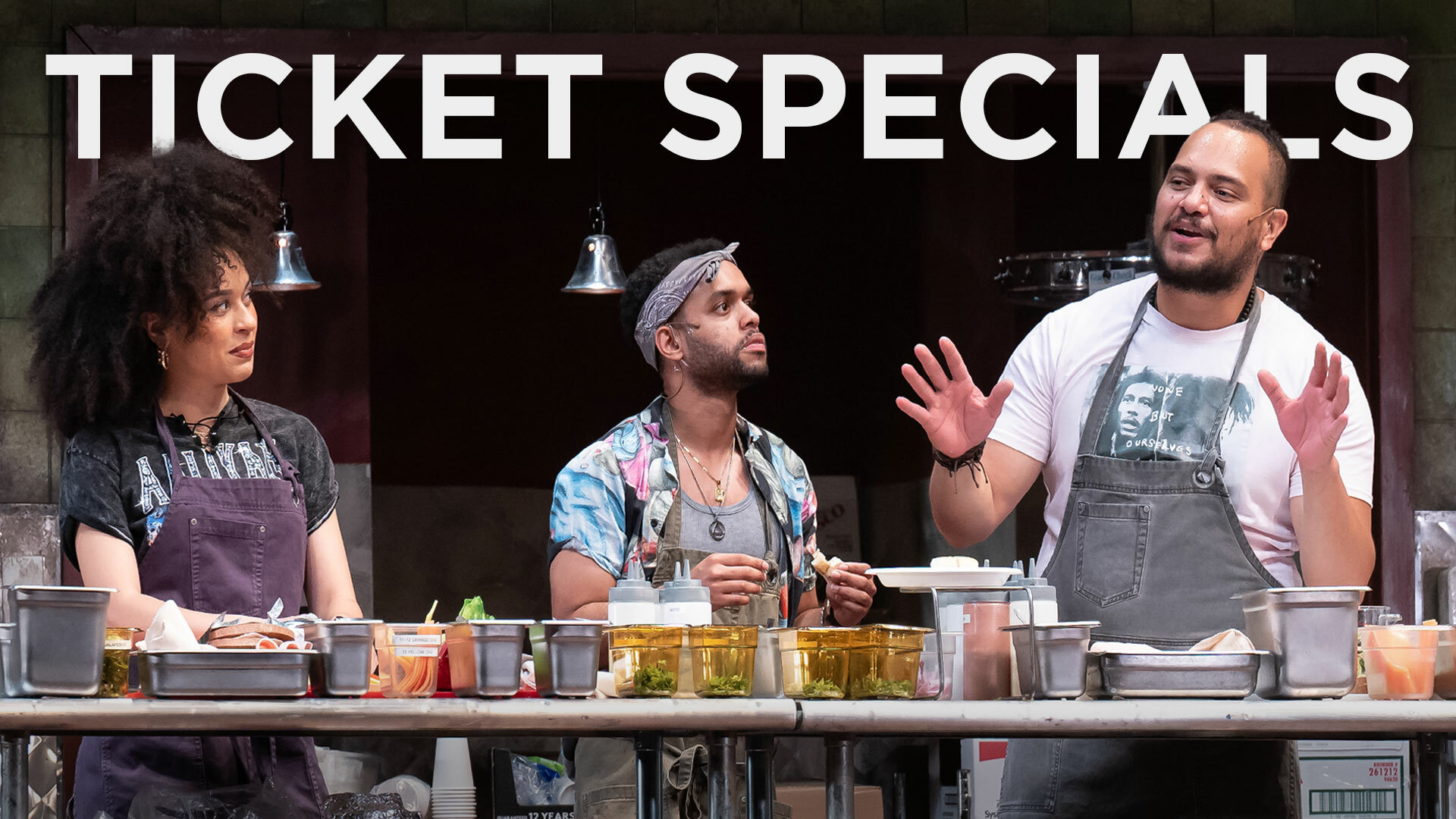 Three line cooks stand in a kitchen, one speaking and gesturing as the others look on. The words "Ticket Specials" appear above them.